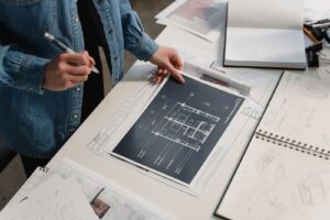 Una progettista in giacca di jeans rivede la pianta di un appartamento sul tavolo da disegno, tra schizzi e taccuini