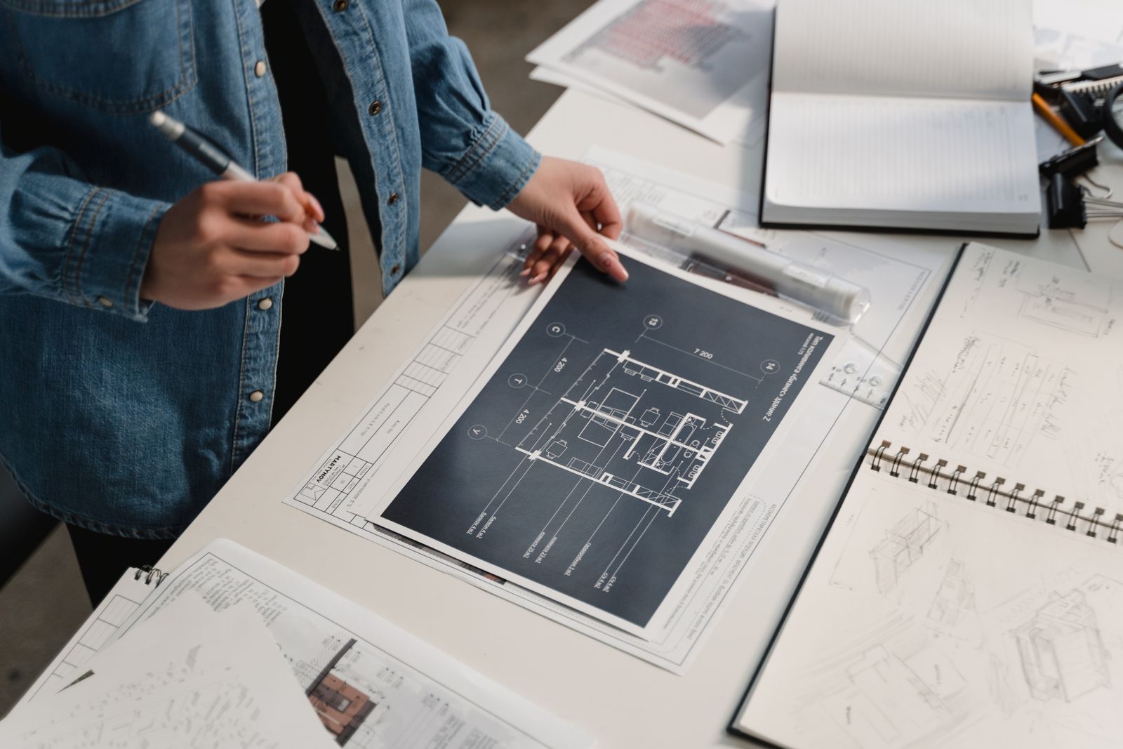 Una progettista in giacca di jeans rivede la pianta di un appartamento sul tavolo da disegno, tra schizzi e taccuini