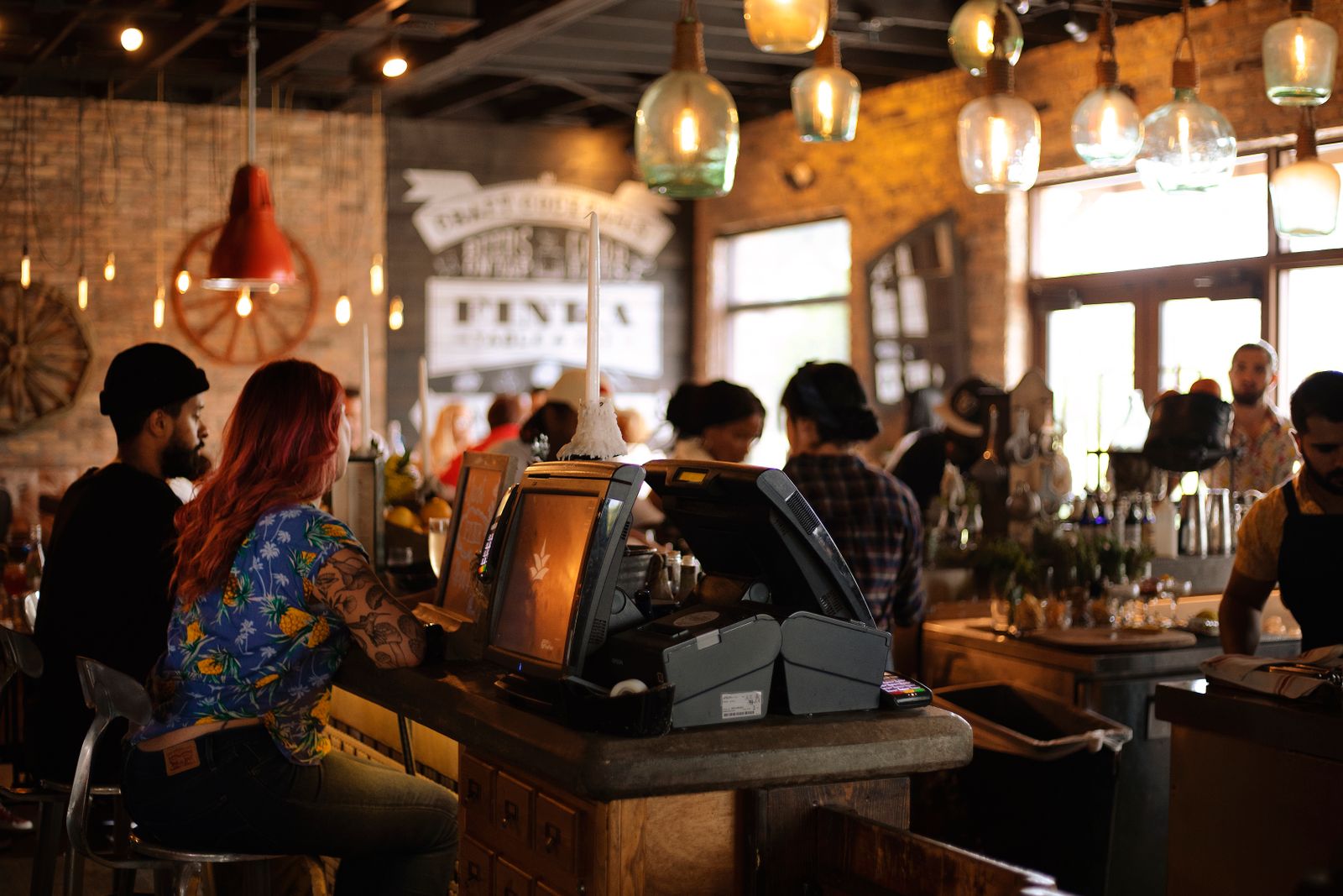 Clienti seduti al bancone di un bar affollato con luci calde e baristi al lavoro
