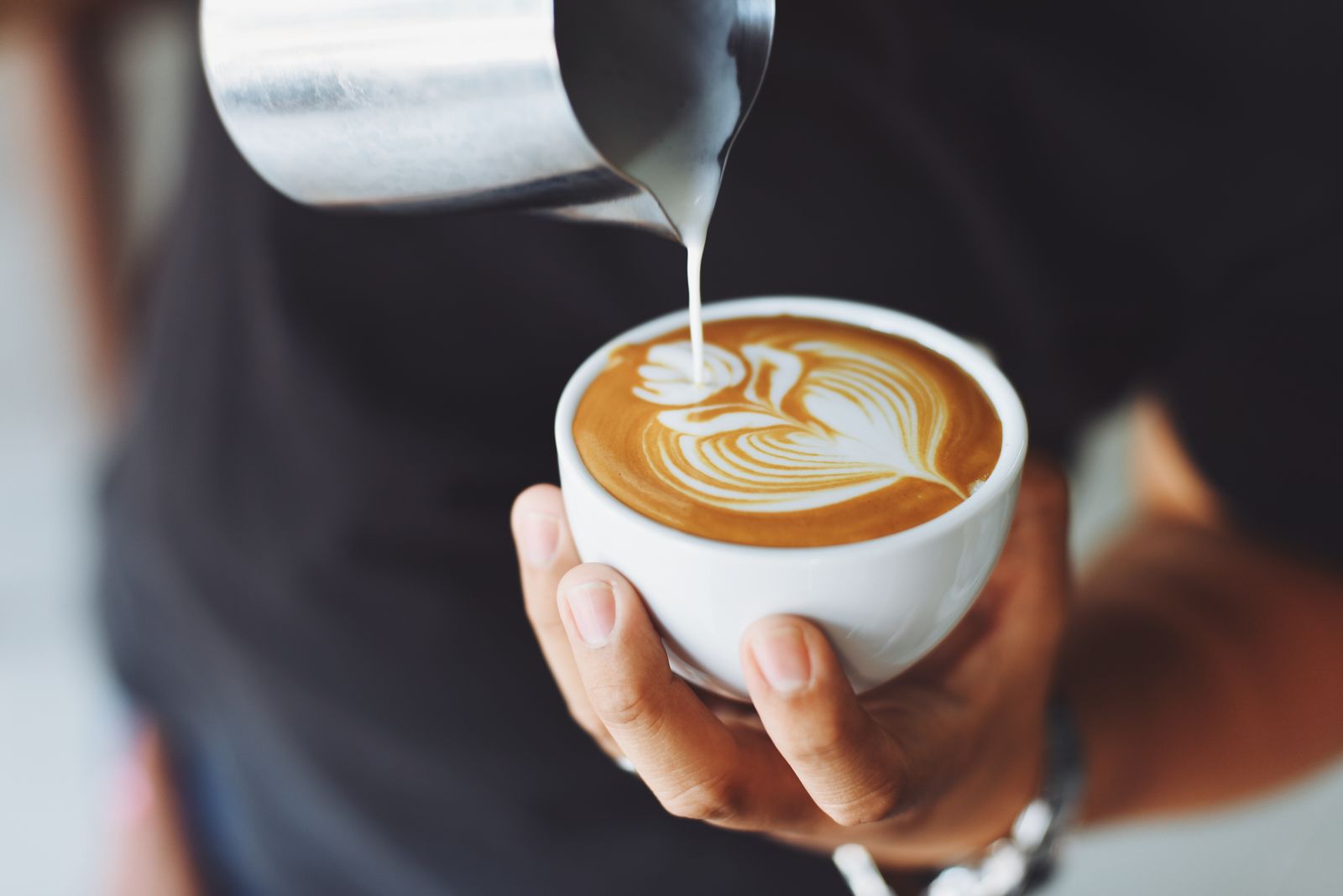 Barista versa il latte montato in una tazza di cappuccino disegnando una foglia sulla schiuma