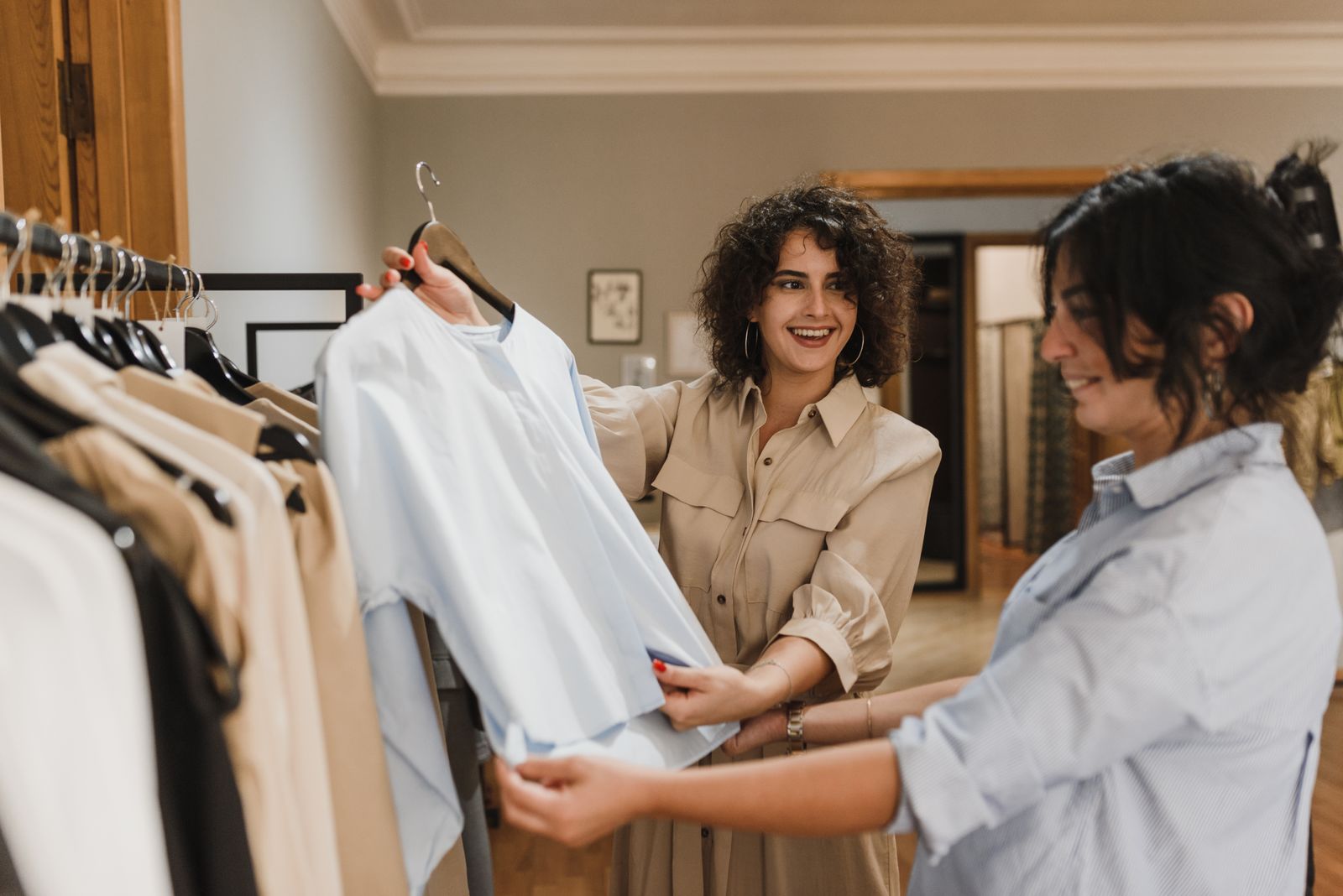 Commessa sorridente mostra una camicia azzurra a una cliente tra gli appendiabiti di una boutique di abbigliamento donna