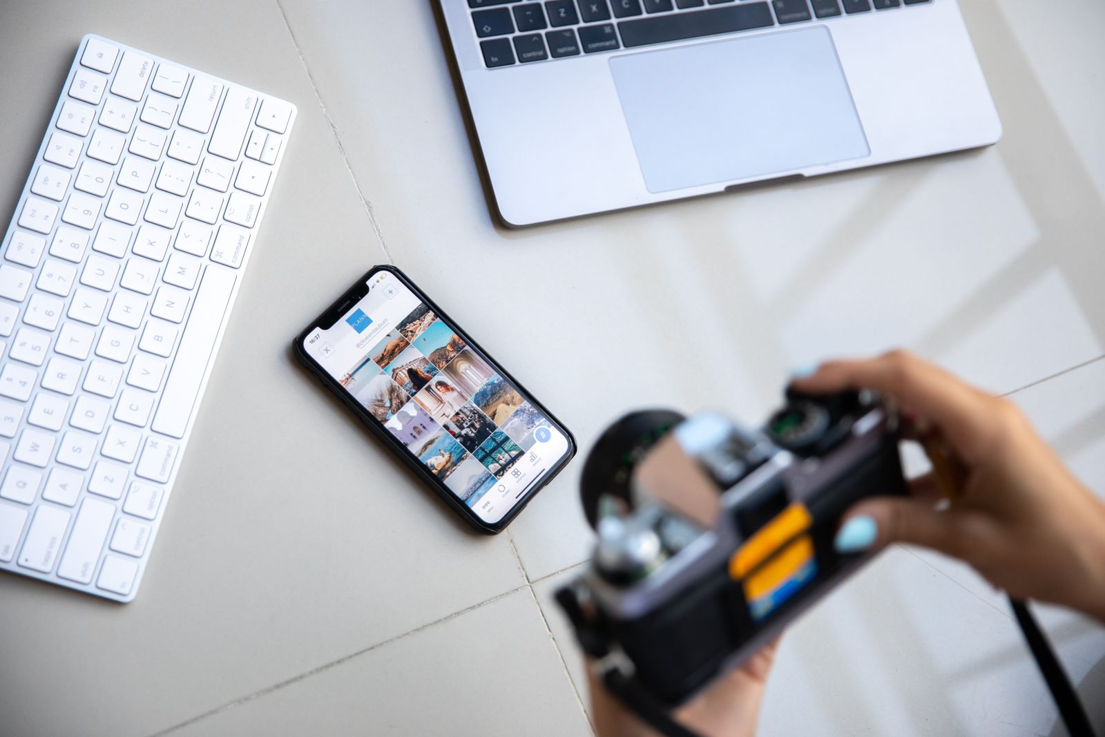Fotocamera in mano, smartphone con una galleria di foto e computer su un tavolo chiaro: il materiale per preparare un contenuto