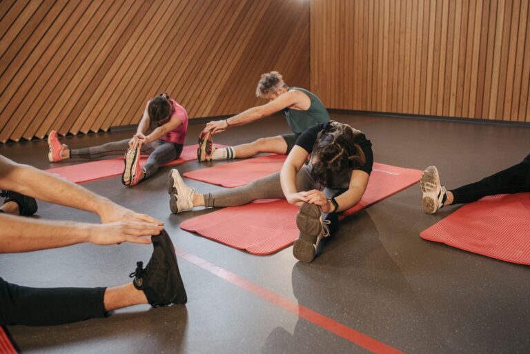 Un gruppo di persone fa stretching sui tappetini rossi durante un corso in palestra