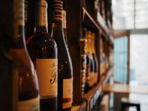 Bottiglie di vino allineate sugli scaffali di legno di un'enoteca, con la luce di una finestra sullo sfondo