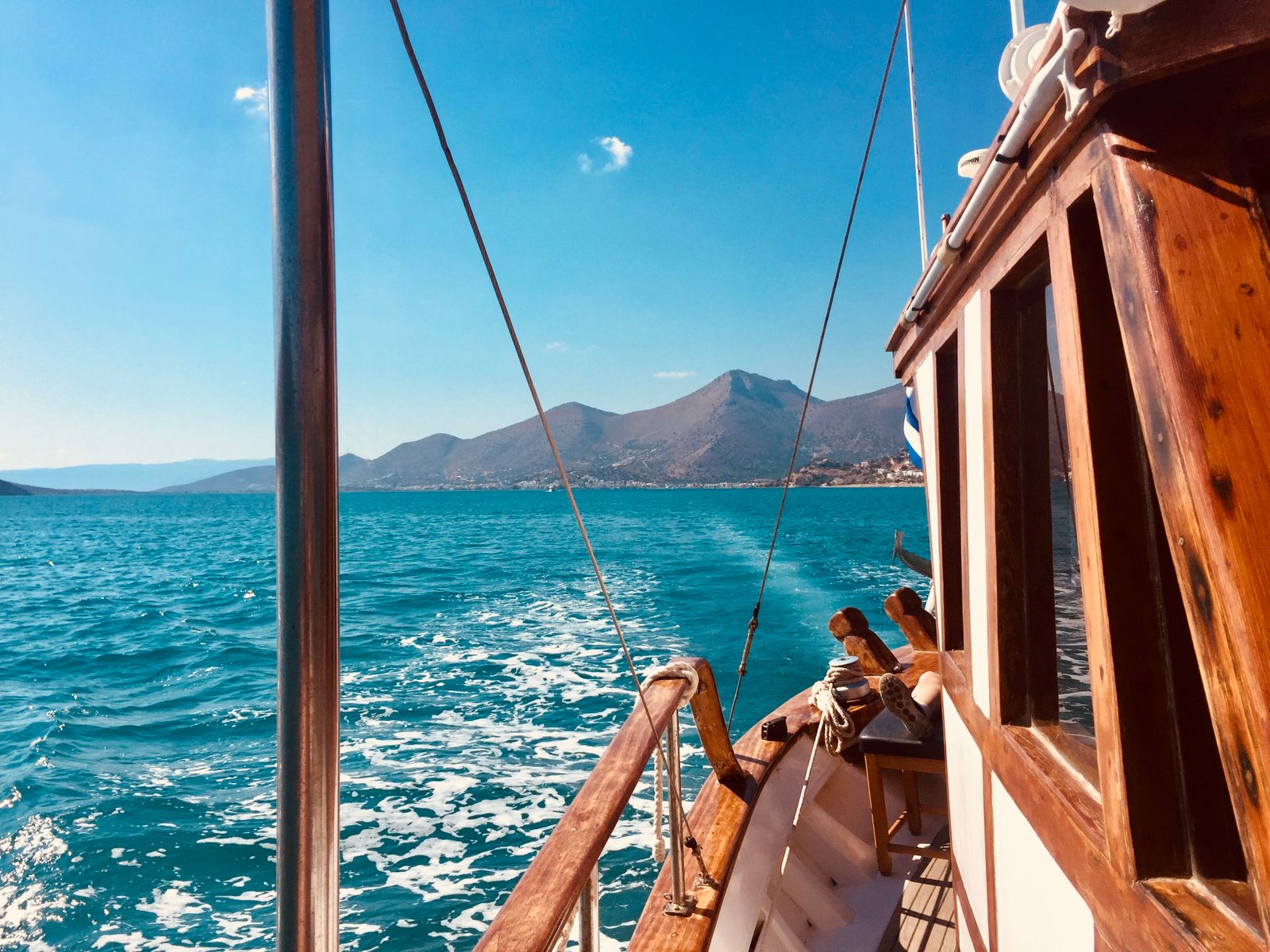 Vista dal ponte di una barca di legno in navigazione, con il mare e le montagne sulla costa