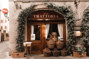Ingresso di una trattoria italiana con porta in legno, rampicanti e damigiane impagliate