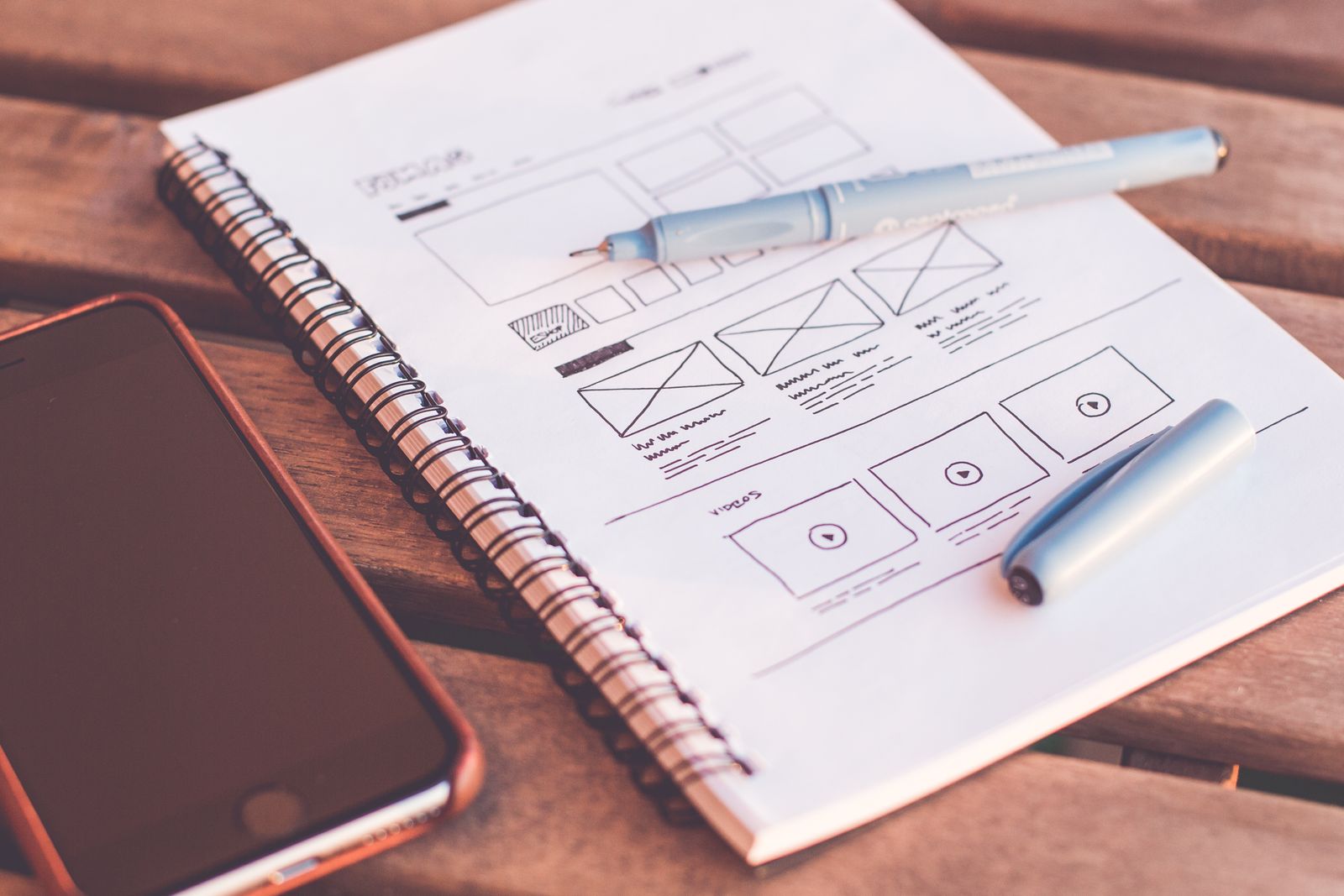 Quaderno ad anelli con lo schizzo a mano della struttura di una pagina web, una penna e uno smartphone su un tavolo di legno