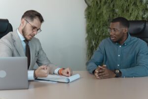 Un consulente in giacca esamina dei documenti al tavolo dell’ufficio mentre un cliente lo ascolta