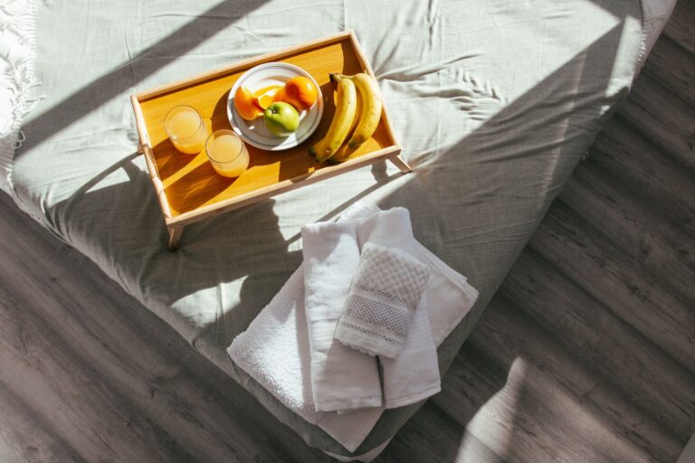 Vassoio con frutta e succhi su un letto illuminato dal sole del mattino, con asciugamani piegati per l'ospite