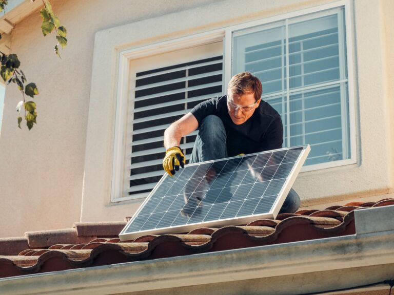 Installatore con occhiali protettivi e guanti che posa un pannello fotovoltaico su un tetto di coppi
