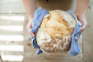 Mani che reggono una grossa pagnotta appena sfornata avvolta in un canovaccio a righe azzurre