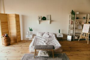 Monolocale arredato per affitti brevi con letto, pavimento in legno, scaffali e paravento in legno chiaro