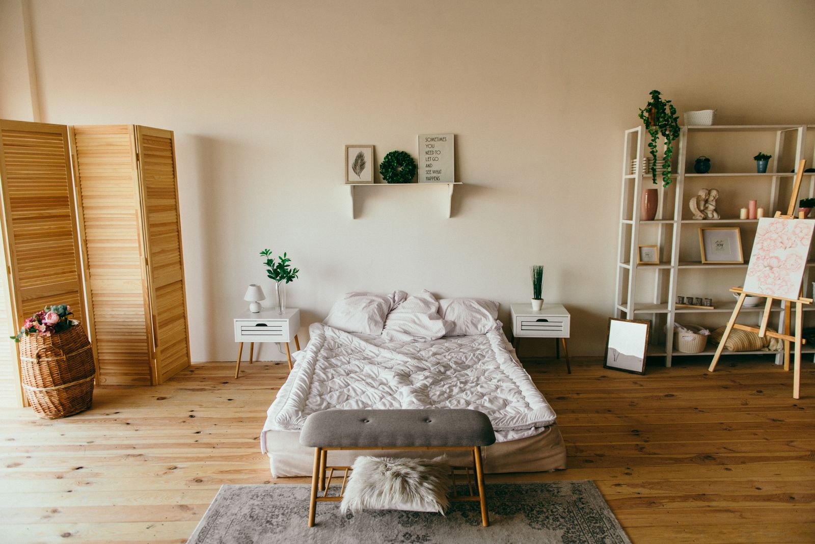 Monolocale arredato per affitti brevi con letto, pavimento in legno, scaffali e paravento in legno chiaro