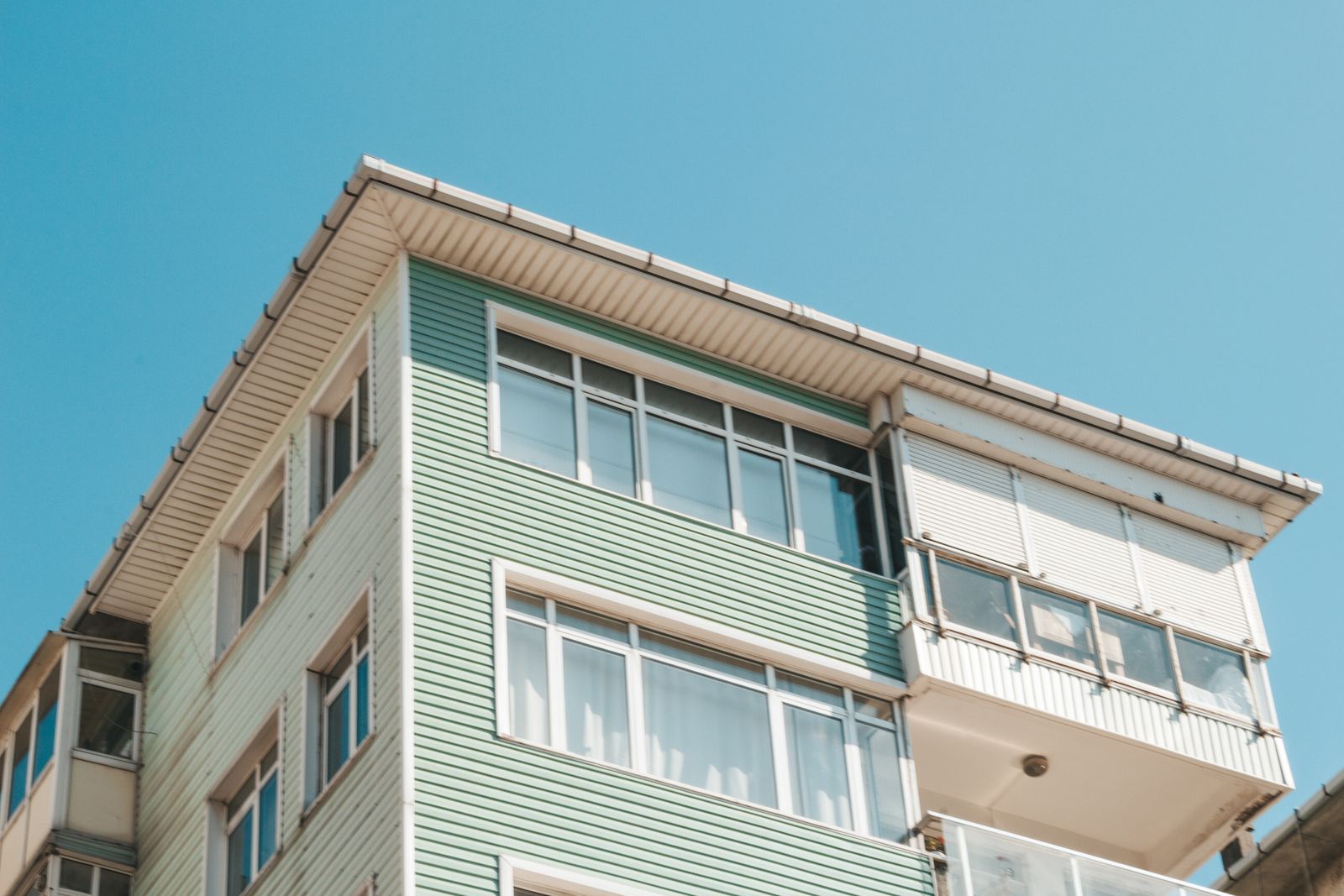Facciata di un palazzo residenziale con finestre e verande in PVC bianco sotto un cielo azzurro
