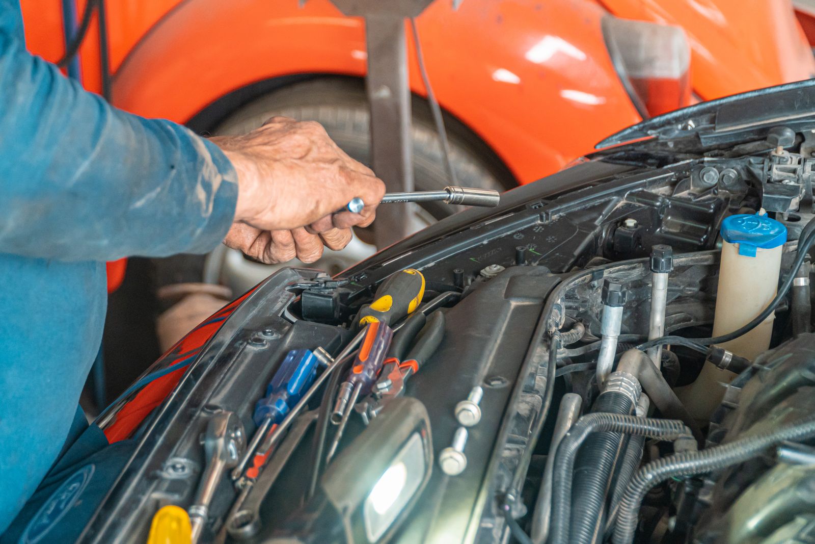 Meccanico che lavora con una chiave nel vano motore di un’auto aperta in officina, con cacciaviti appoggiati sul radiatore