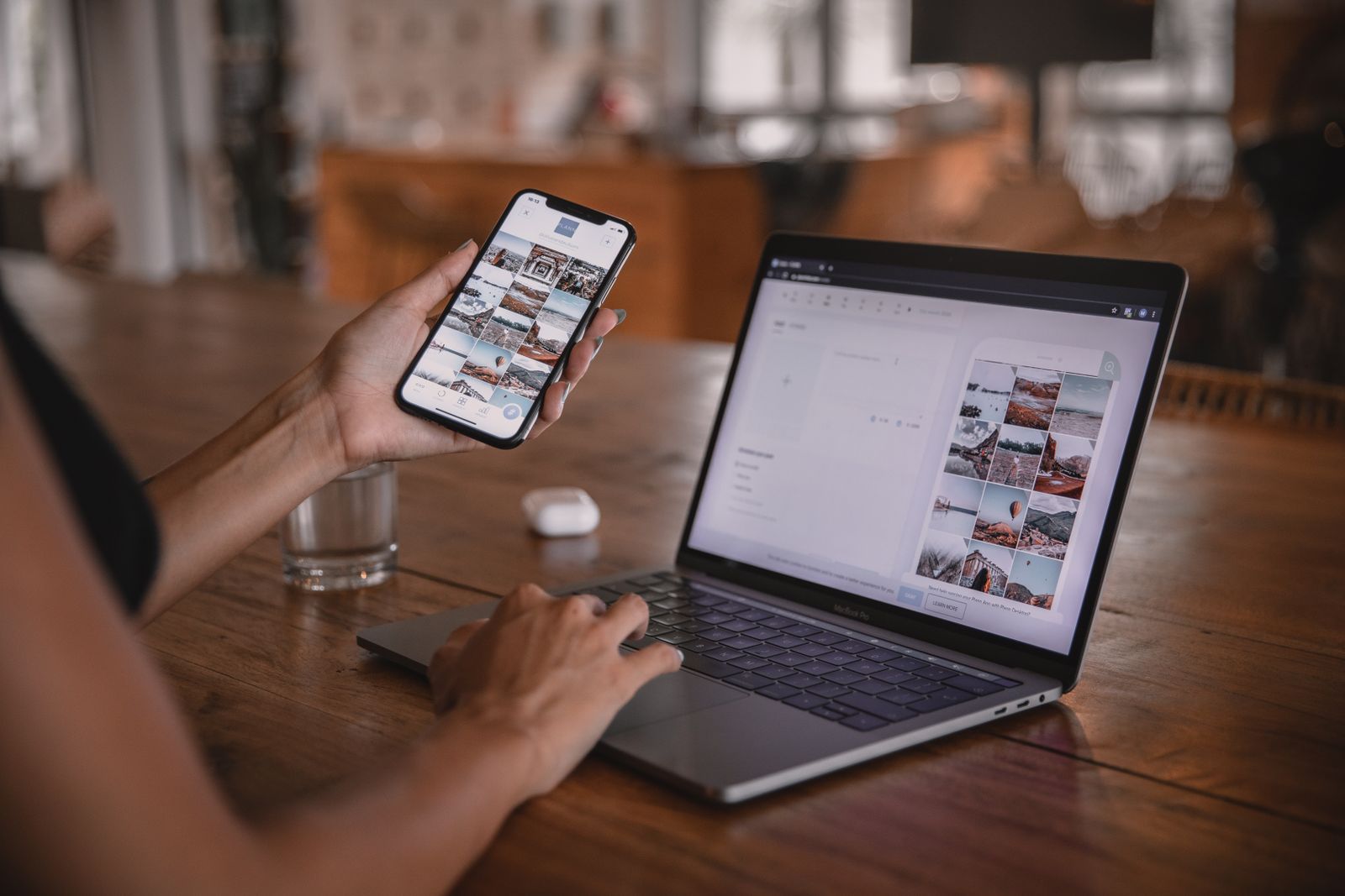 Donna a un tavolo di legno con lo smartphone in mano e il portatile aperto mentre prepara contenuti per i social