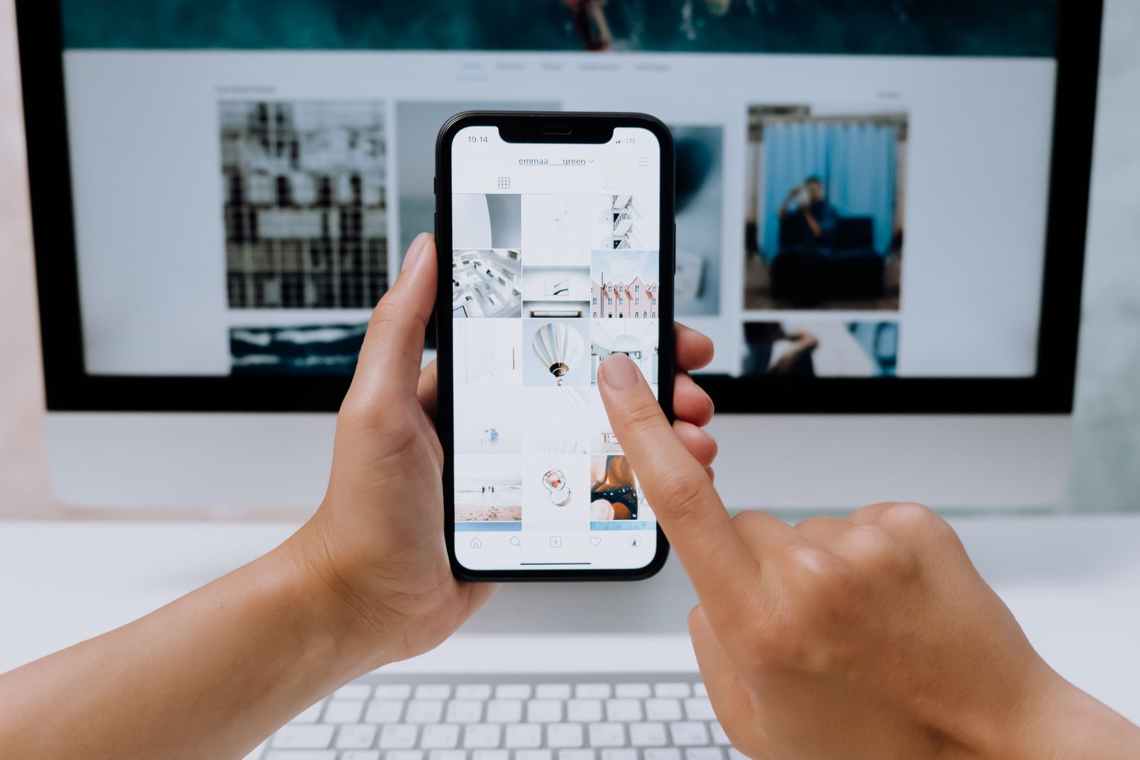 Mani che scorrono un profilo social su uno smartphone davanti a un computer