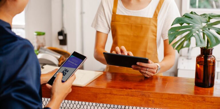 Cliente con lo smartphone al bancone di un bar mentre la titolare usa un tablet