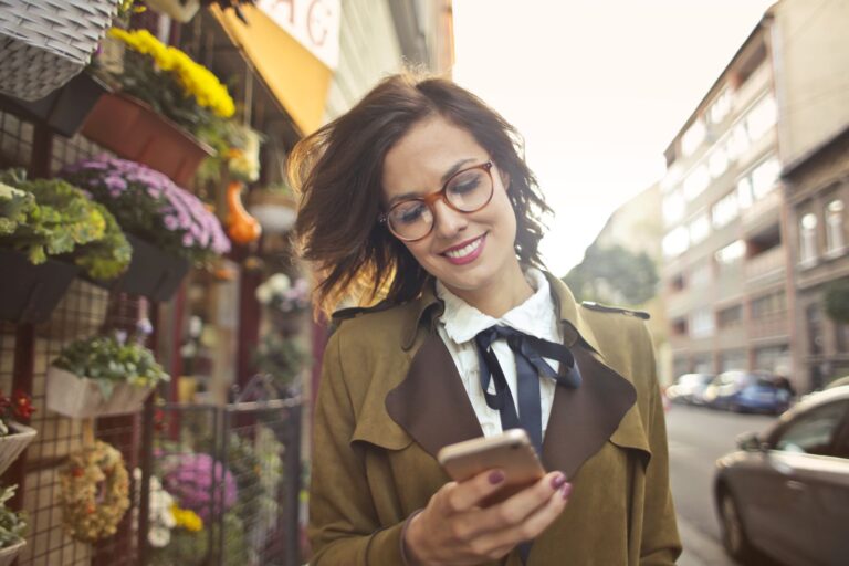 Donna davanti a un negozio di fiori che consulta lo smartphone per strada