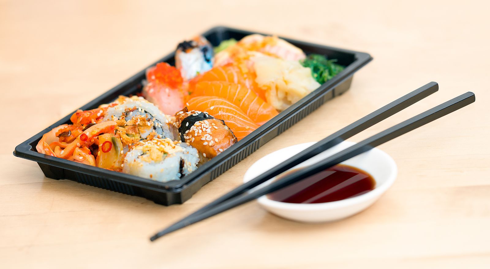 Vaschetta da asporto con uramaki, nigiri e sashimi di salmone, bacchette e ciotola di salsa di soia