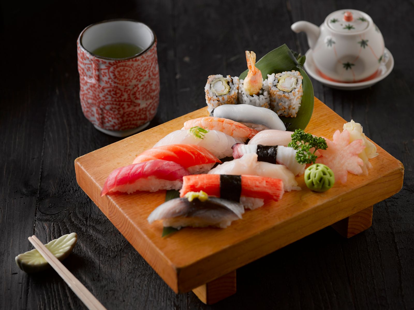 Nigiri e sushi misto su un tagliere di legno con tazza di tè verde e bacchette