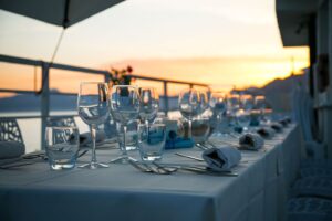 Lunga tavolata apparecchiata per un ricevimento su una terrazza sul mare al tramonto, con calici e tovaglioli azzurri